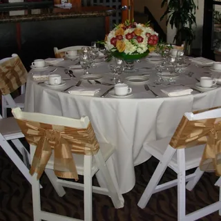Round table with a white tablecloth, gold sashes and white folding chairs