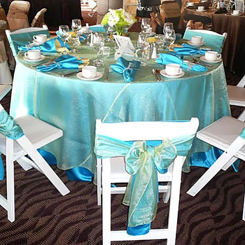 Round table in a turquoise linen with white folding chairs and sashes