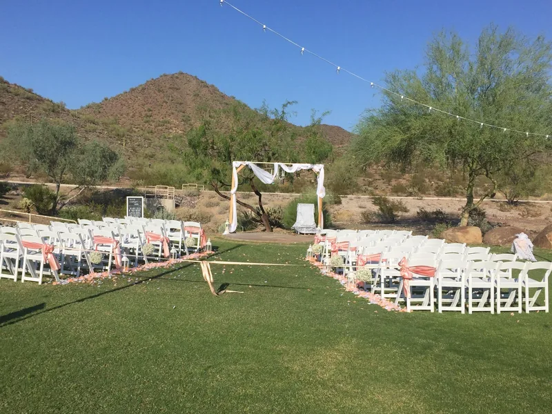 Rows of white folding chairs on a lawn set for an outdoor wedding ceremony, with desert mountains behind