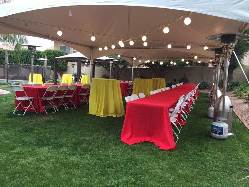 Globe string lights hanging inside a white tent over tables with red and yellow linens