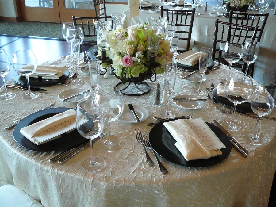Round reception table with an ivory textured tablecloth, folded napkins and place settings