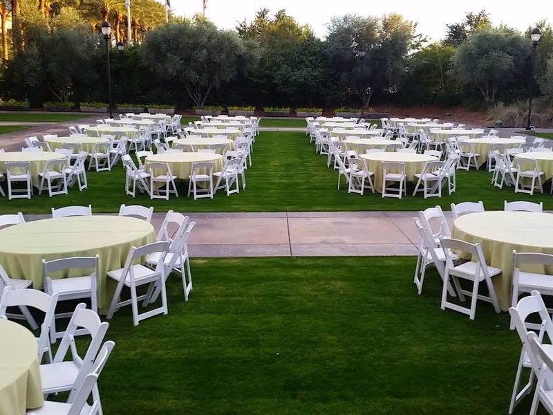 Round tables with white linens and white folding chairs set up on a green lawn for an outdoor party