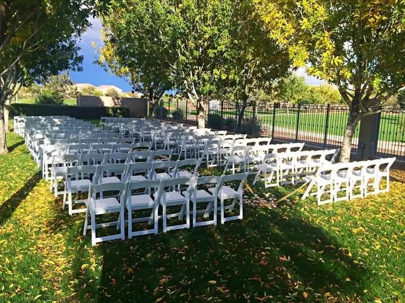 Rows of white folding chairs set up on a shaded lawn for an outdoor gathering