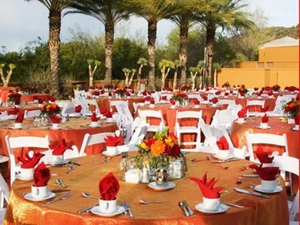 Round tables with orange floor-length linens and white folding chairs at an outdoor reception